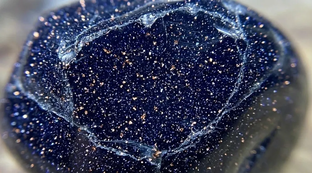 Macro close-up of blue sandstone showing copper metallic particles suspended inside glass matrix